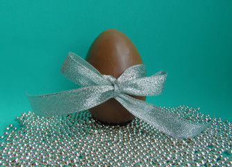 Obraz na płótnie Canvas Chocolate Easter egg with a bow and beads on a green background