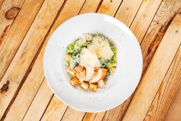 Fresh caesar salad in white plate, wooden background