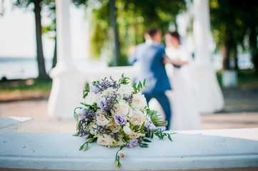 Pair of groom and bride on the back focus and bouquet of flowers lies on the railing