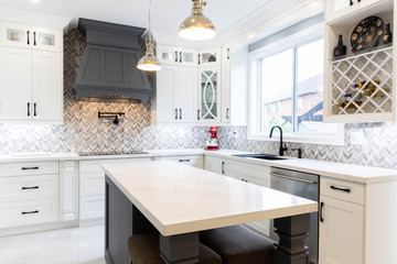Contemporary Style Kitchen in New Luxury Home with white cabinets, cool gray island, stainless steel appliances with a double oven, cooktop, sink and faucet