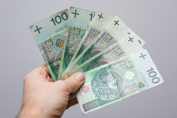 close up of one banknote with a face value of PLN 100 Polish money, zloty held  in the hands of a women on a grey background