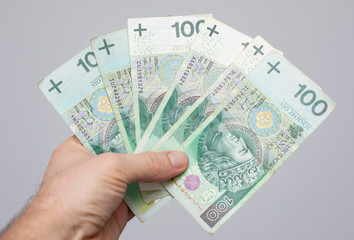 close up ofbanknote with a face value of PLN 100 Polish money, zloty held  in the hands of a women on a grey background