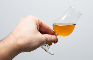 close-up of  whiskey tasting glass with whiskey held in a hand on a gray background