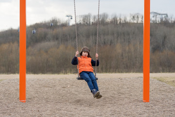 Obraz premium Joyful boy on the playground on a swing.