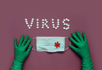 Inscription VIRUS from white pills, hands in protective gloves hold medical mask