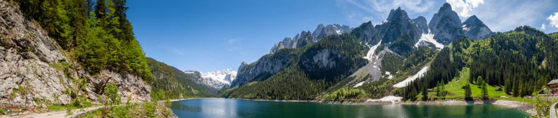 Fototapeta na wymiar Famous Lake Gosau and Gosaukamm with Mount Dachstein. Spring is here! The snow is melting and spring brings the luscious green back to nature. The sun is about to hide behind the high peaks.