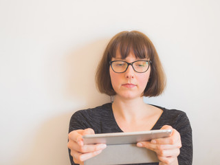 Horizontal portrait of a middle-aged Caucasian woman in casual clothes wearing black frame eyeglasses and using tablet