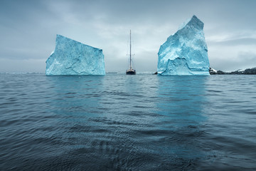 sailing yacht rides through strait between two huge icebergs in Antarctica