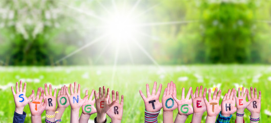 Children Hands Building Colorful Word Stronger Together. Green Grass Meadow As Background