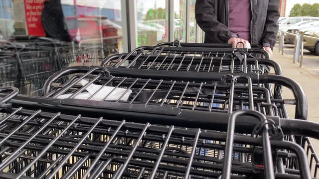 A man wipes the handle of a shopping cart outside of a grocery store. Cleaning surfaces became a common sight during the coronavirus COVID-19 pandemic of 2020.	