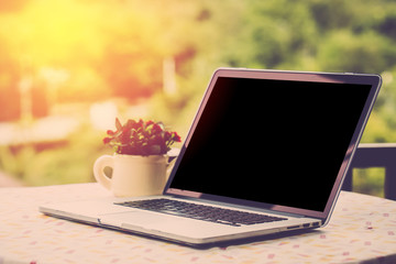 Blank screen computer PC on table with garden view background. Vintage filter.