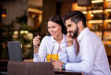 Businessman and businesswoman looking at the laptop while they are both drinking orange juice.