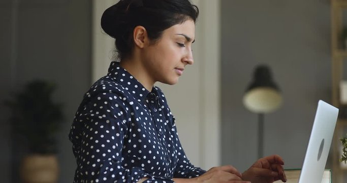 Side view concentrated young indian businesswoman working on computer at office or home, communicating with clients. Focused successful hindu female international company employee busy with project.