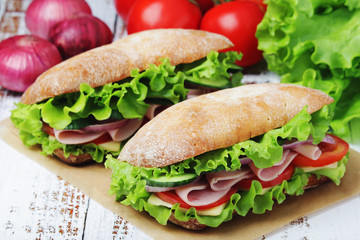 Two sandwiches with fresh vegetables, ham and cheese in ciabatta bread	