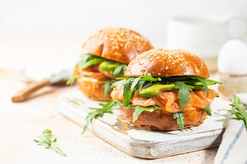Burger sandwich with salmon, cream cheese, avocado and arugula on a light background, concept diet food, sandwich take away, healthy fast food