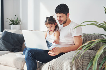 Happy father with his daughter spending free time with laptop at home together