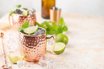 Cold Moscow Mules cocktail with ginger beer, vodka, lime. White stone background.