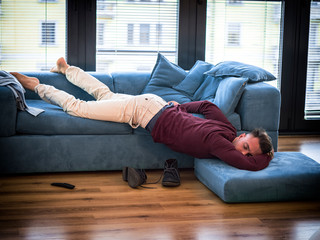 Drunk Young Handsome Man Resting on Couch in the Living Room with Head on the Floor.