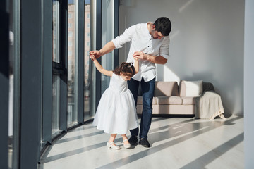 Fototapeta premium Happy father with his daughter in dress learning how to dance at home together