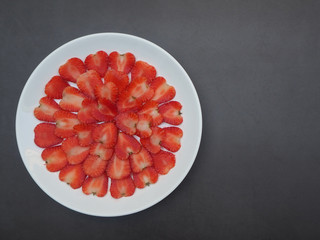 Top view red strawberry ripe piece slice of shape heart in a white dish (plate) on the black cement background with copy space using for design banner healthy or diet food concept.