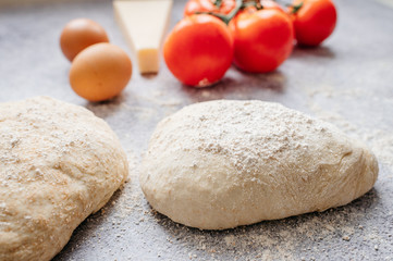 wholemeal dough ball for homemade pizza made on an abstract stone background with ingredients around, tomato, flour, cheese and egg