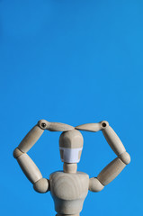 A wooden figure in a medical mask raised his hands to his head. Coronavirus, pandemic and epidemic concept