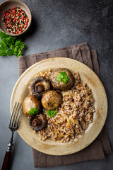 Buckwheat porridge with mushrooms in a plate on black background, top view