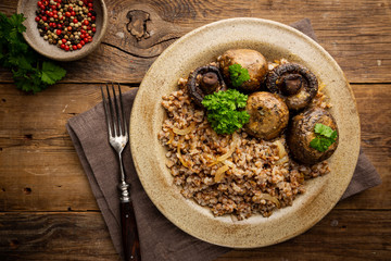 Buckwheat porridge with mushrooms in a plate on wooden table, top view