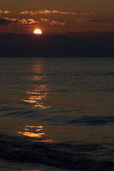 Sunset at the tropical beach, sun behind clouds reflects on water.
