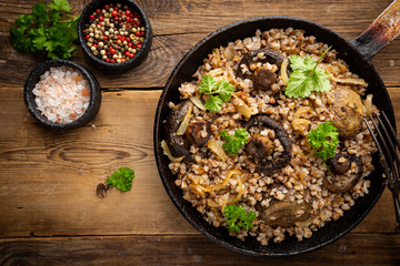 Buckwheat porridge with mushrooms in the frying pan on wooden table, top view