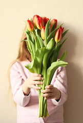 A young girl in a pink blouse is holding a beautiful festive bouquet of fresh red tulips , covering her face with them .Girl gives tulips. A child with flowers in his hands.Selective focus.