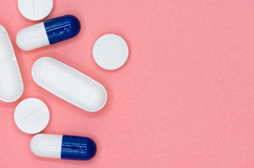 Various white and blue pills on pink background with copy space. Different medical drugs . 