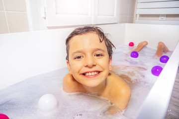 Portrait of a boy play with toys and soap on the belly in the bath water at home