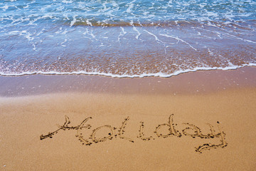 Holiday inscription on a tropical sandy beach with waves and foam on a background.