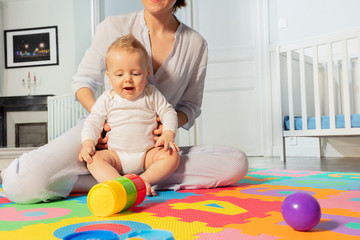 Young mother play and interact with toddler baby boy in the nursery sitting on the floor