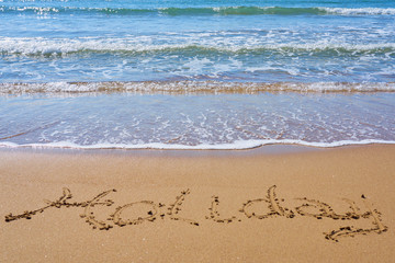 Holiday inscription on a tropical sandy beach with waves and foam on a background.