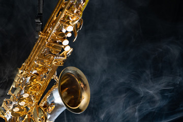 Golden shiny alto saxophone on black background with smoke. copy space