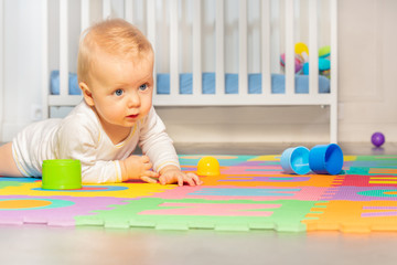 Beautiful baby toddler crawl on the floor of nursery grabbing toys near crib