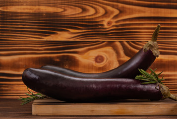 Fresh raw purple eggplants and rosemary leaves on brown wooden background. Vegetables for cooking