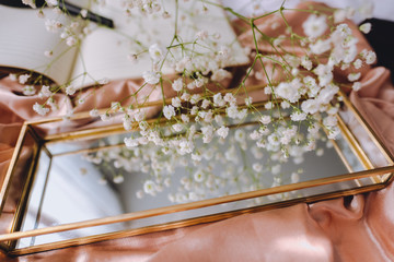 Spring composition, white gypsophila flowers with gold mirror and notebook on the gold satin fabric