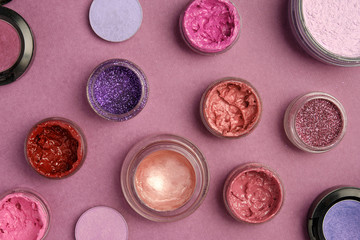 Glitter, lipstick, lip gloss, eye shadow and powder are placed on a plum textured background