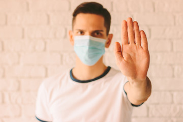 Young healthy man in medical protective mask on face showing stop gesture with his palm. Stop...