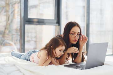 Young mother with her daughter spending weekend together in room and using laptop