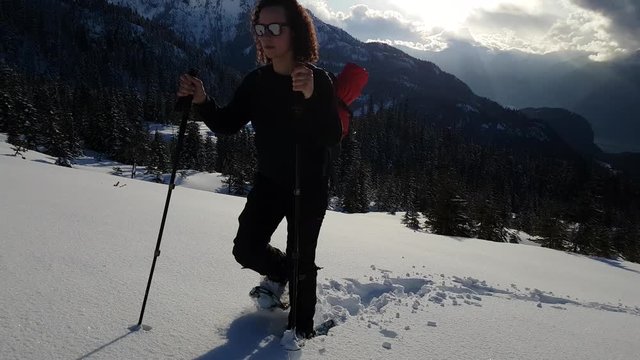 Adventurous Girl Snowshoeing in the snow on top of a mountain during a vibrant and colorful winter evening. Taken on Anif Peak, Squamish, British Columbia, Canada. Concept: explore, adventure