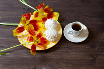 Marshmallow, cup of coffee and tulip flowers on wooden table