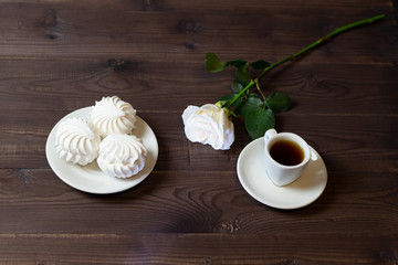 White rose, marshmallow, cup of coffee on brown wooden background