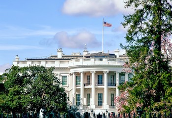 Fototapeta na wymiar The United States White House on a beautiful sunny afternoon with an American flag on the roof with bright blue sunny sky and puffy white clouds.