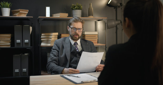 Business looking man reading incoming employee's resume during job interview holding it in his hands