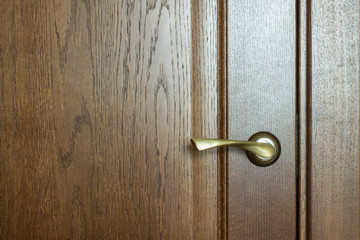 Obraz premium Fragment of a wooden brown textured door with a metal door handle close-up with copy space. Concept: hygiene, coronavirus