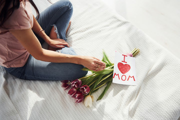 Top view of woman that sits on bed with bouquet of flowers and post card with heart pictures on it